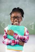 Portrait of happy schoolgirl holding file in classroom