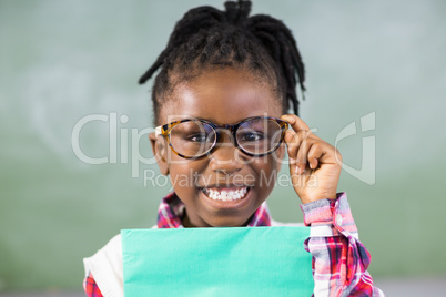 Portrait of happy schoolgirl holding file in classroom