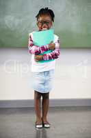 Portrait of happy schoolgirl holding file in classroom