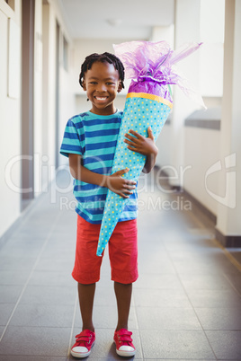 Portrait of smiling schoolboy holding gift in corridor