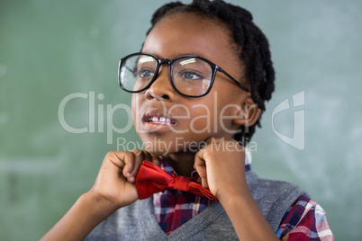 Thoughtful schoolboy adjusting a bow tie in classroom