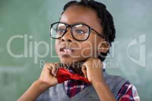Thoughtful schoolboy adjusting a bow tie in classroom