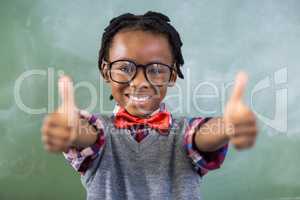 Portrait of smiling schoolboy showing thumbs up in classroom