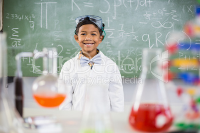 Smiling schoolboy standing in classroom with chemical flask in foreground