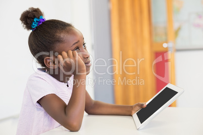 Thoughtful schoolgirl with digital tablet in classroom