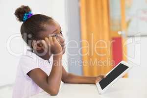 Thoughtful schoolgirl with digital tablet in classroom