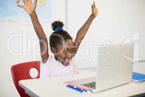 Excited schoolgirl with laptop in classroom