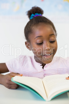 Smiling school girl reading book in classroom