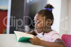 School girl reading book in classroom
