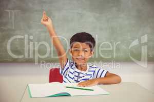 Portrait of schoolboy raising his hand in classroom