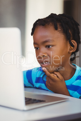 Thoughtful schoolboy using laptop in classroom