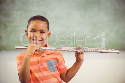 Portrait of smiling schoolboy playing flute in classroom