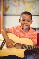 Portrait of smiling schoolboy playing guitar in classroom