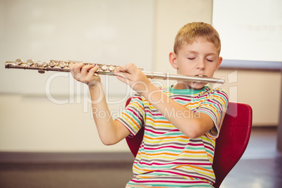 Schoolboy playing flute in classroom