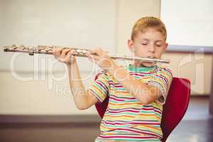 Schoolboy playing flute in classroom