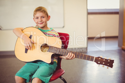 Portrait of smiling schoolboy playing guitar in classroom