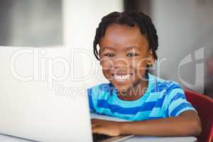 Schoolboy sitting on chair and using laptop at school