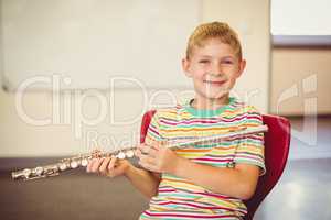 Portrait of smiling schoolboy playing flute in classroom