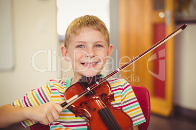 Portrait of smiling schoolboy playing violin in classroom