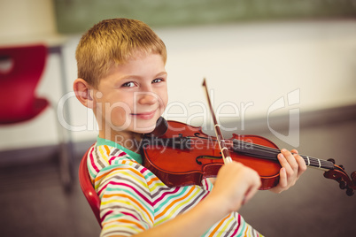 Portrait of smiling schoolboy playing violin in classroom