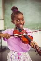 Portrait of smiling schoolgirl playing violin in classroom