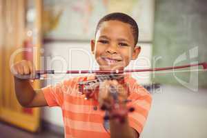 Portrait of smiling schoolboy playing violin in classroom