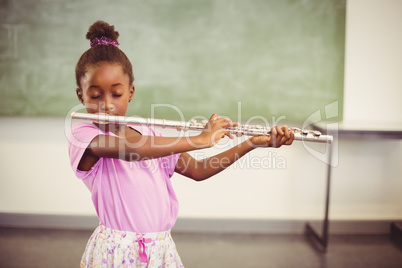 Schoolgirl playing flute in classroom