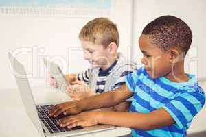 School kids using a laptop and digital tablet in classroom