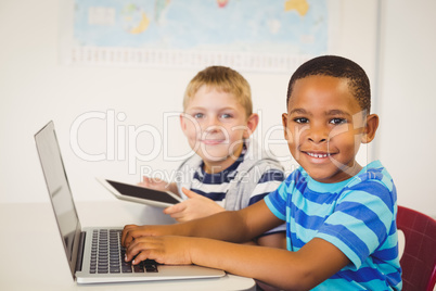 Portrait of kids using a laptop and digital tablet in classroom Portrait of kids using a laptop and digital tablet in classroom