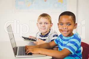 Portrait of kids using a laptop and digital tablet in classroom