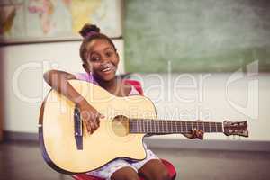 Portrait of smiling schoolgirl playing guitar in classroom