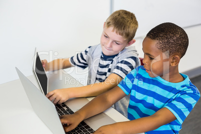 School kids using a laptop and digital tablet in classroom