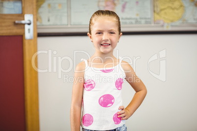 Portrait of cute girl standing with hand on hip in classroom