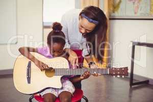 Teacher assisting a girl to play a guitar in classroom