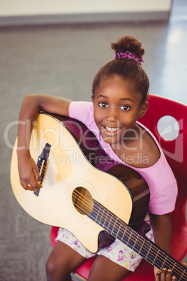 Portrait of smiling schoolgirl playing guitar in classroom