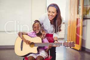 Teacher assisting a girl to play a guitar in classroom