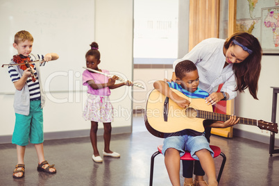 Teacher assisting a kids to play a musical instrument in classroom