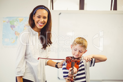 Teacher assisting a schoolboy to play a violin in classroom