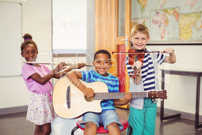 Portrait of smiling kids playing guitar, violin, flute in classroom