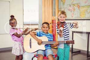 Portrait of smiling kids playing guitar, violin, flute in classroom