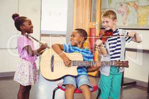 Smiling kids playing guitar, violin, flute in classroom