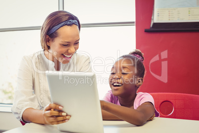 Teacher and school girl using digital tablet in classroom