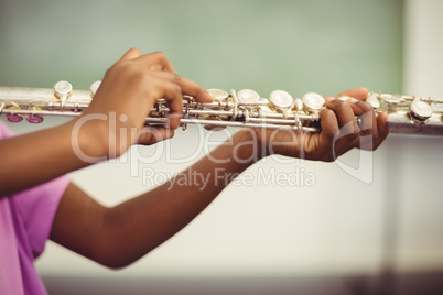 Schoolgirl playing flute in classroom