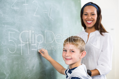 Portrait of teacher assisting boy in doing addition on chalkboard