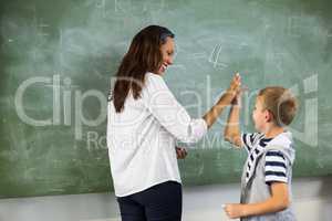 Happy teacher and school boy giving high five in classroom