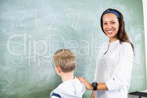 Smiling teacher assisting boy in doing addition on chalkboard