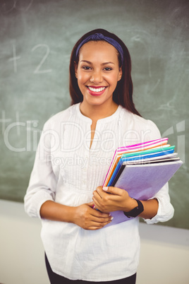 Portrait of smiling school teacher holding books in classroom