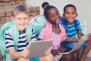 Portrait of kids using a laptop and digital tablet on stairs