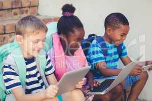 Smiling kids using a laptop and digital tablet on stairs