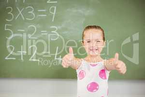Portrait of smiling schoolgirl showing thumbs up in classroom